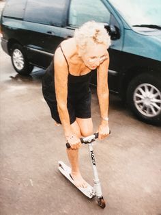 an older woman riding on top of a scooter in front of a van