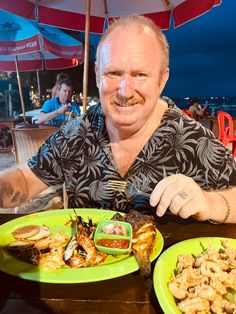 a man sitting at a table with plates of food in front of him and an umbrella