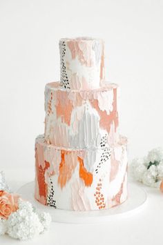 a three tiered cake with orange and white icing on a plate next to flowers