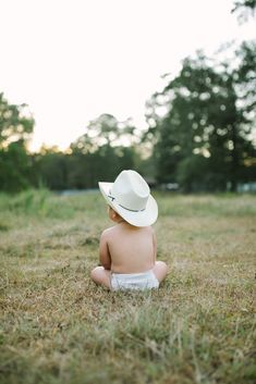 a baby sitting in the grass wearing a white hat and diaper on his back