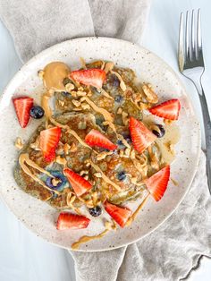 a white plate topped with fruit and granola covered in peanut butter next to a fork