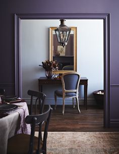 a dining room with purple walls and chairs in the corner, along with a mirror on the wall