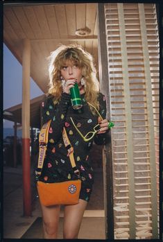 a woman drinking from a green cup while standing in front of a building