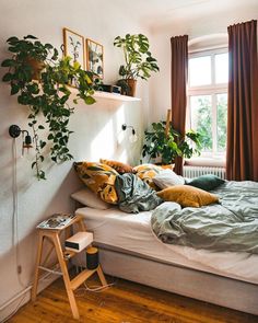 an unmade bed with lots of plants on the headboard and shelves above it