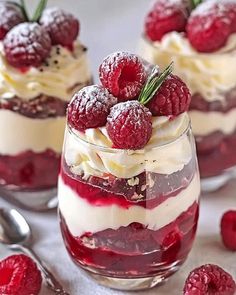 three desserts with raspberries and whipped cream in small glass dishes next to spoons