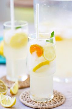 two glasses filled with lemonade and limes on a table next to sliced lemons