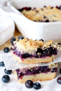 blueberry crumb bars stacked on top of each other next to a bowl of fresh blueberries