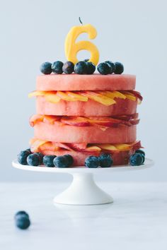 a birthday cake with blueberries and oranges on it is sitting on a white pedestal