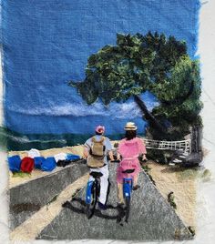 two people riding bikes down a road next to the ocean