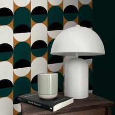 a white lamp sitting on top of a wooden table next to a book and cup