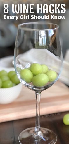 a wine glass filled with green grapes on top of a wooden table