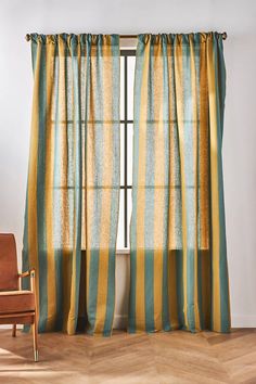 a chair sitting in front of a window with striped curtains on the windowsills