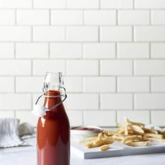 a glass bottle filled with ketchup sitting on top of a counter next to french fries