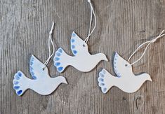 three ceramic doves hanging from strings on a wooden surface, one is blue and the other is white