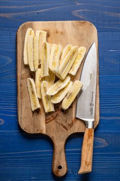 sliced bananas are on a cutting board next to a knife and wooden block against a blue background