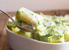 a spoon full of pasta and broccoli in a white casserole dish