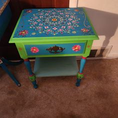 a blue and green table with flowers painted on it's top, sitting in a room