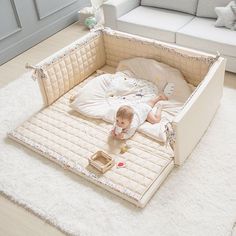 a baby laying in a bed on top of a white rug next to a couch