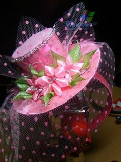 a pink and black polka dot hat with flowers on it's side sitting on a table