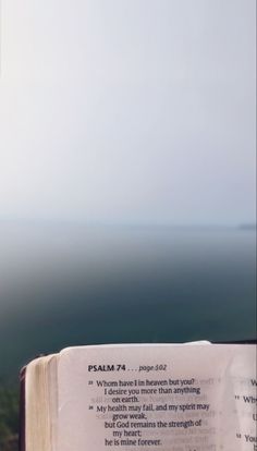 an open book sitting on top of a wooden table next to the ocean and sky