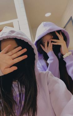 two young women wearing hoodies and covering their faces with hands while standing in front of a mirror