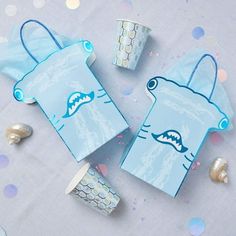 two blue paper bags with shark faces on them and confetti scattered around it