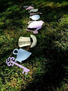 a line of cut out metal objects in the grass with scissors and coffee mugs on them