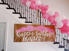 a happy birthday sign with pink balloons on the stair case next to a set of black railings