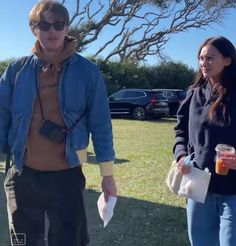 a man and woman standing next to each other on a field with cars in the background