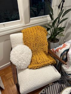 a chair with a blanket on it next to a potted plant and a window