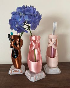 three vases with flowers in them sitting on a table next to a toothbrush holder