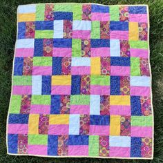 a patchwork quilt on the grass with green grass in the foreground and pink, blue, yellow and purple squares