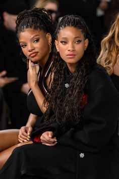 two women sitting next to each other at a fashion show, one with her hand on her chin