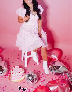 a woman sitting on a chair in front of a cake and party balloons with confetti