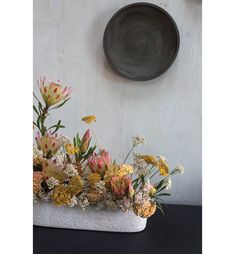 a vase filled with lots of flowers next to a wall mounted plate on the wall