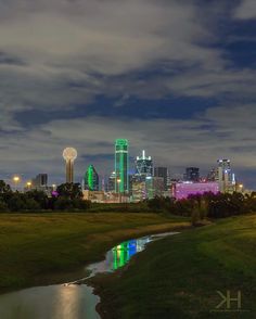 the city skyline is lit up in green and purple at night, as well as water