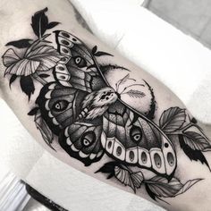 a black and white photo of a moth tattoo on the arm, with leaves around it