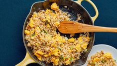 a pan filled with rice and vegetables on top of a plate next to a wooden spoon