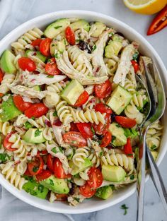 a white bowl filled with pasta salad next to sliced oranges and cucumbers