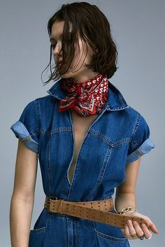 a woman wearing a denim jumpsuit with a red bandanna around her neck and brown belt