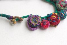 a multicolored crocheted necklace with beads and bells on a white surface