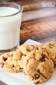 three chocolate chip cookies on a napkin next to a glass of milk