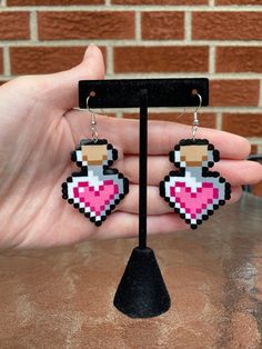 a pair of pixel heart earrings is shown in front of a brick wall and black stand