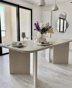 a dining room table and chairs with flowers in vases on the end, next to an open patio door