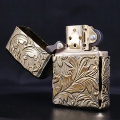 a gold colored flask style lighter with an intricate design on the front and side