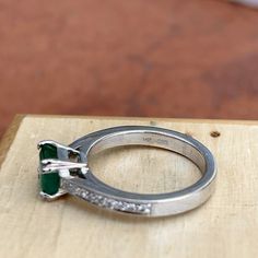 an engagement ring sitting on top of a piece of wood with a green stone in the middle