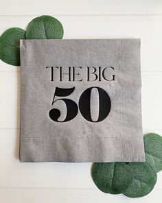 a napkin that says the big 50 on it next to some green leafy leaves