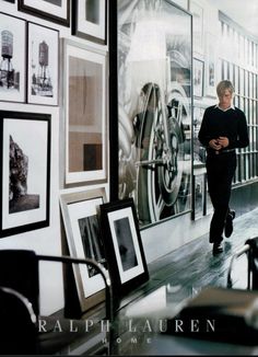 a man is walking down the hallway in front of some pictures and framed photographs on the wall