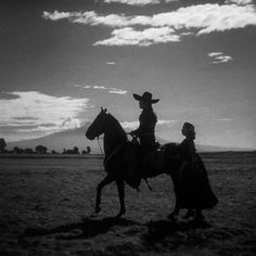 black and white photograph of two people riding horses in the desert with clouds behind them