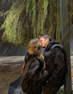 a man and woman kissing under an umbrella in the rain